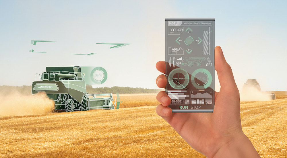 Farmer uses a futuristic transparent smartphone to control autonomous harvester. Smart farming concept.